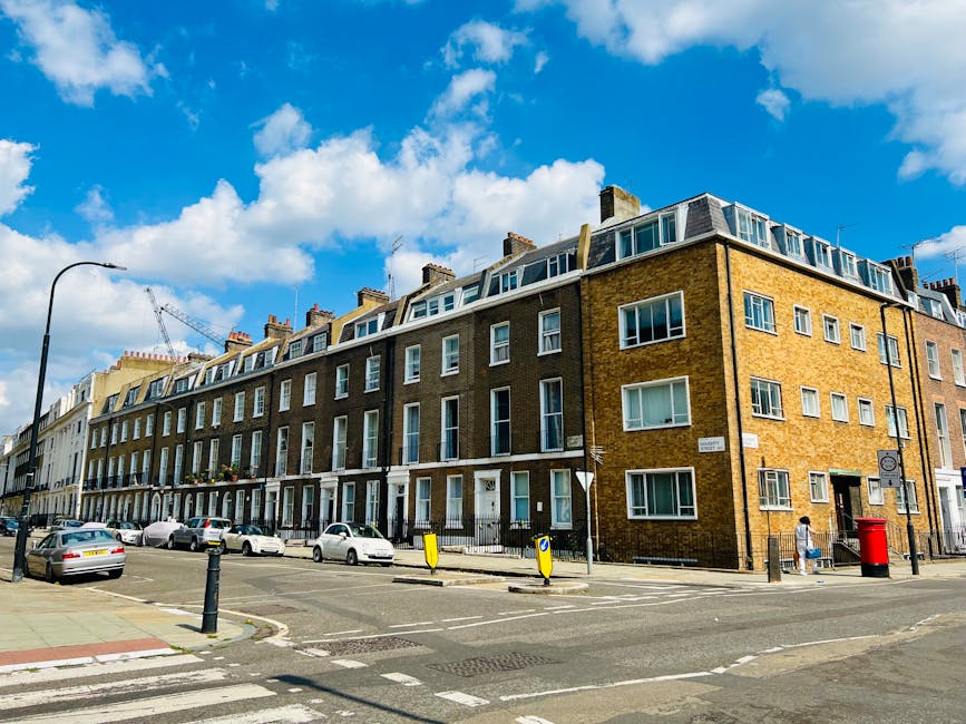 Exterior view of a multi-story Victorian-style building featuring dark brick walls and ornate white decorative moldings around tall sash windows, which are set in symmetrical rows. The windows have bl